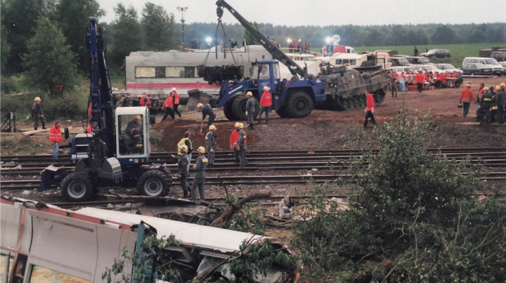 Auf Schienen und dem Gelände drum herum stehen Fahrzeuge und Einsatzkräfte in roten und blauen Anzügen. Vorne im Bild liegt ein umgekippter Zugwagen. (Quelle: THW) Auf Schienen und dem Gelände drum herum stehen Fahrzeuge und Einsatzkräfte in roten und blauen Anzügen. Vorne im Bild liegt ein umgekippter Zugwagen.