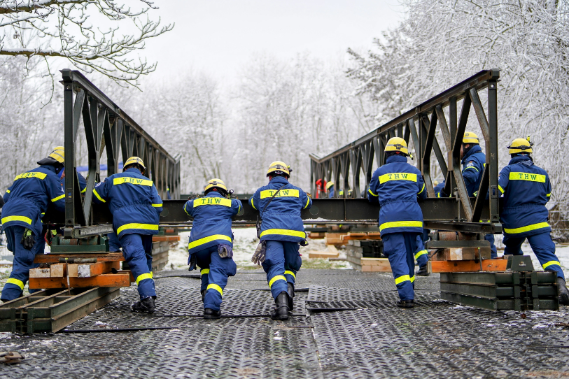 Menschen in Einsatzkleidung schieben eine neu zusammengebaute Brücke voran.