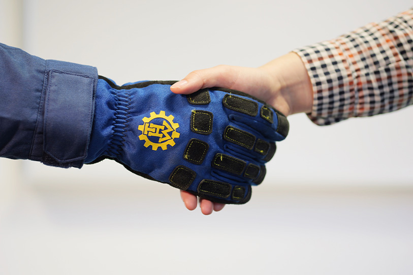 Two people shake hands, one hand is in a blue THW glove. (Source: THW) Two people shake hands, one hand is in a blue THW glove.